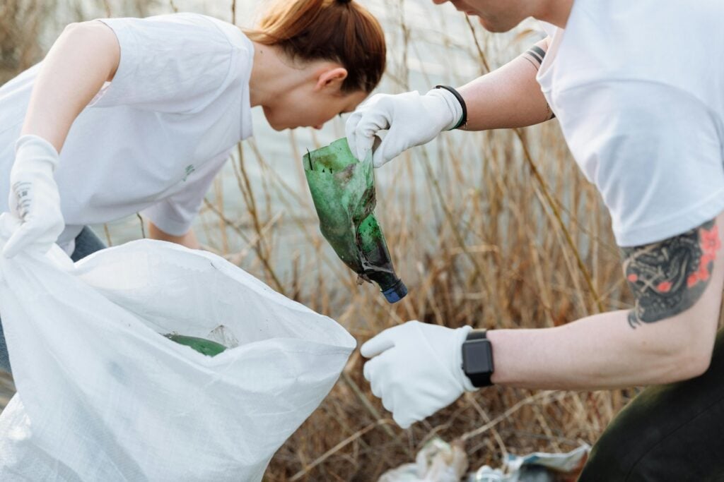 People with gloved hands picking out trash near a swamp