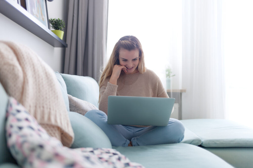 Happy woman at home using laptop sitting on sofa, online working