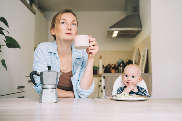 mom pondering and holding cup while baby eats next to her