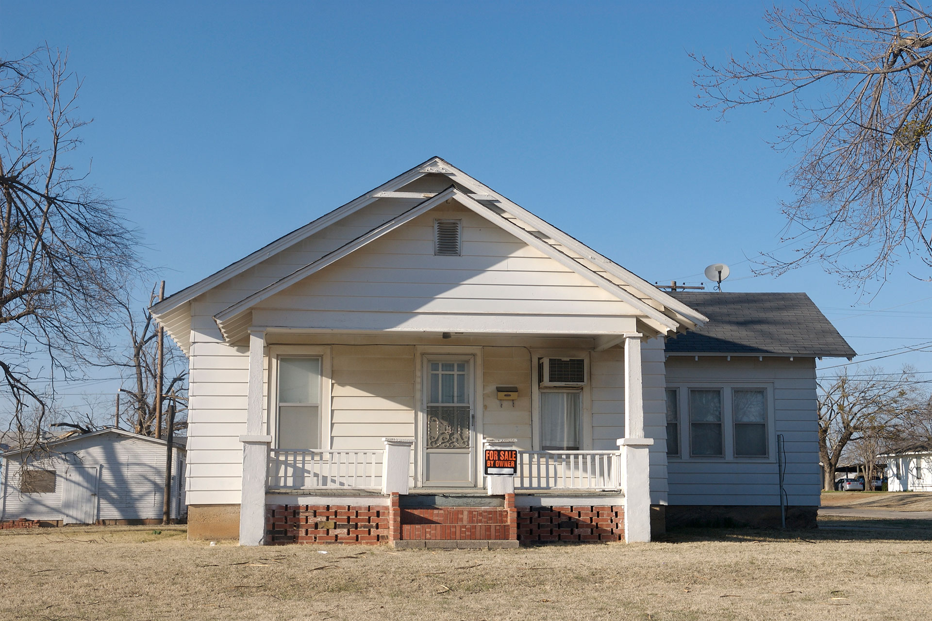 Small white cottage style house with for sale by owner sign on front porch.