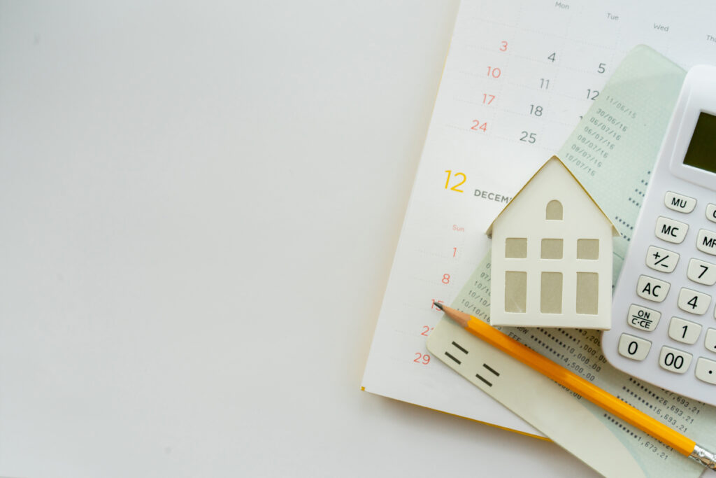 A calendar, miniature house model, calculator, and financial documents arranged on a desk, symbolizing mortgage planning and homeownership.