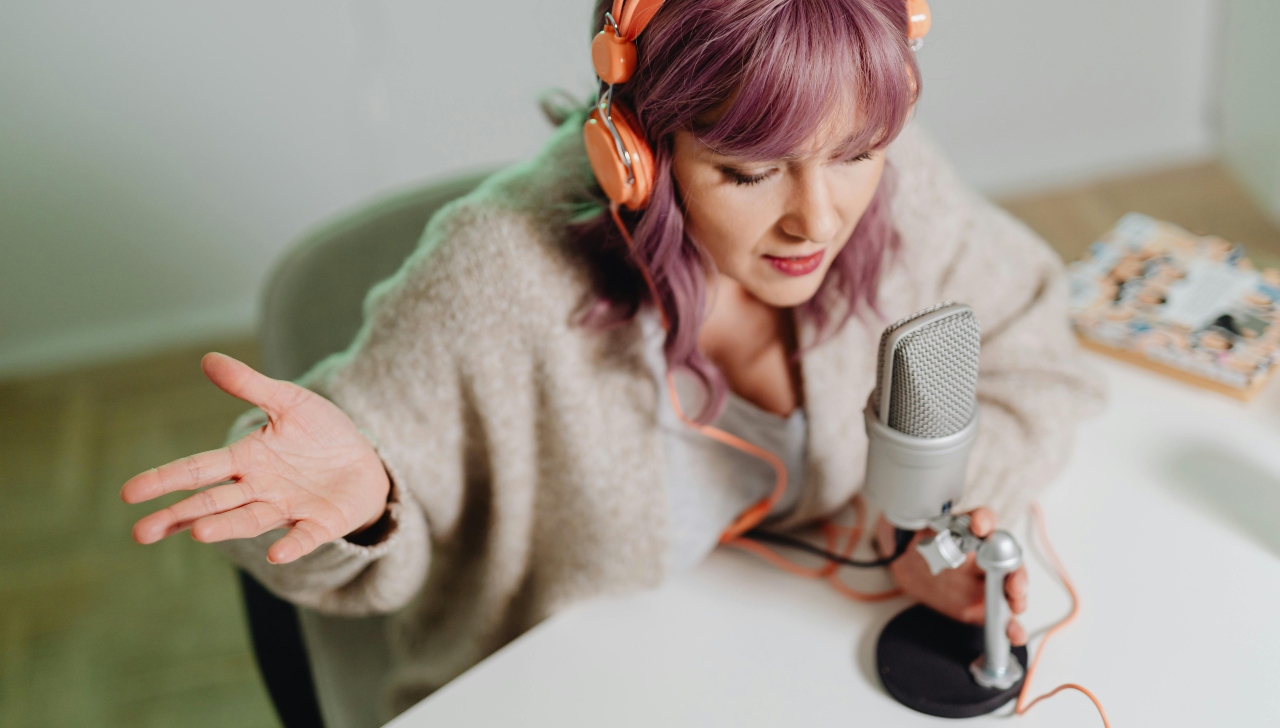 girl with pink hair sitting in a green chair speaking into a microphone