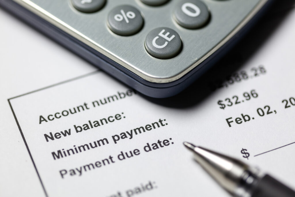 Close-up of a calculator on top of a billing statement showing account balance, minimum payment, and payment due date.